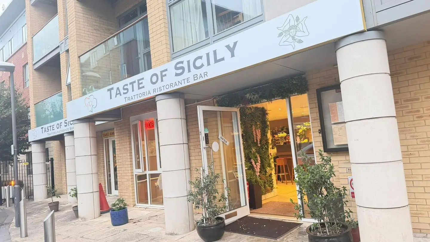 The Taste of Sicily shopfront: the Trattoria Ristorante Bar sign with its Sicilian emblem, and the door open onto a warm-lit entrance